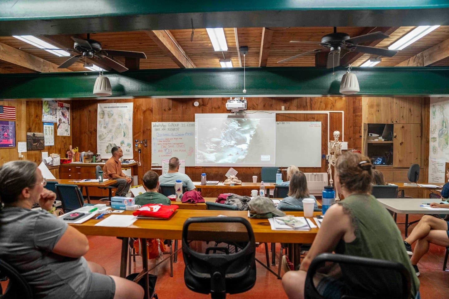 Instruktör leder diverse vuxna i inomhusutbildning med projektor.